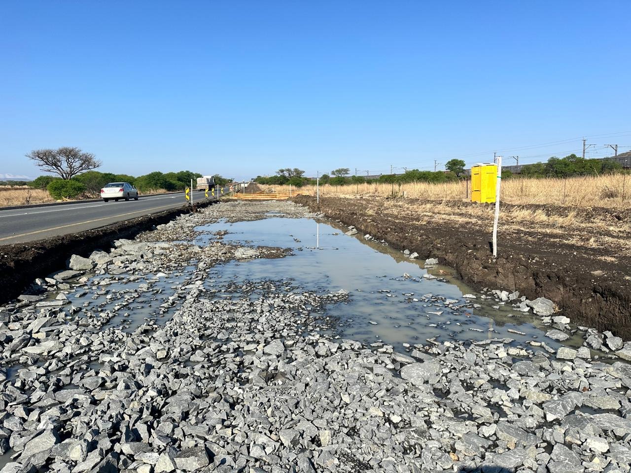 Roadside works with rock fill, standing water and a portable toilet beside the carriageway